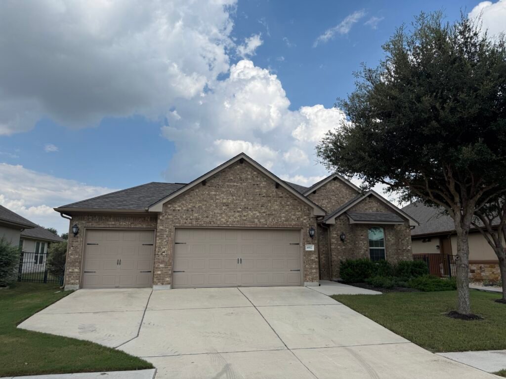 a single-story brick Round Rock Texas home with three car garage showing a newly-installed asphalt roof